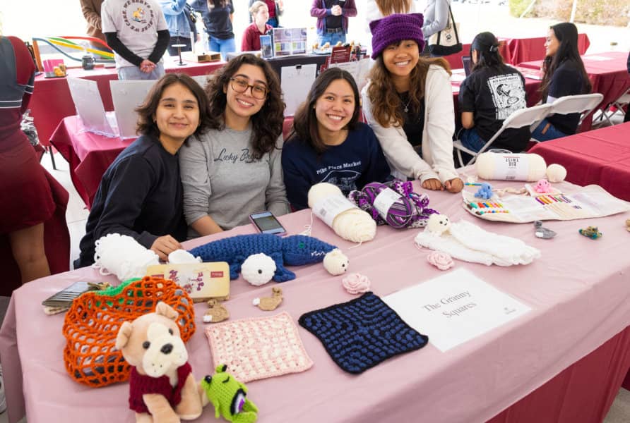 a group of women sitting at a table with crochet crafts