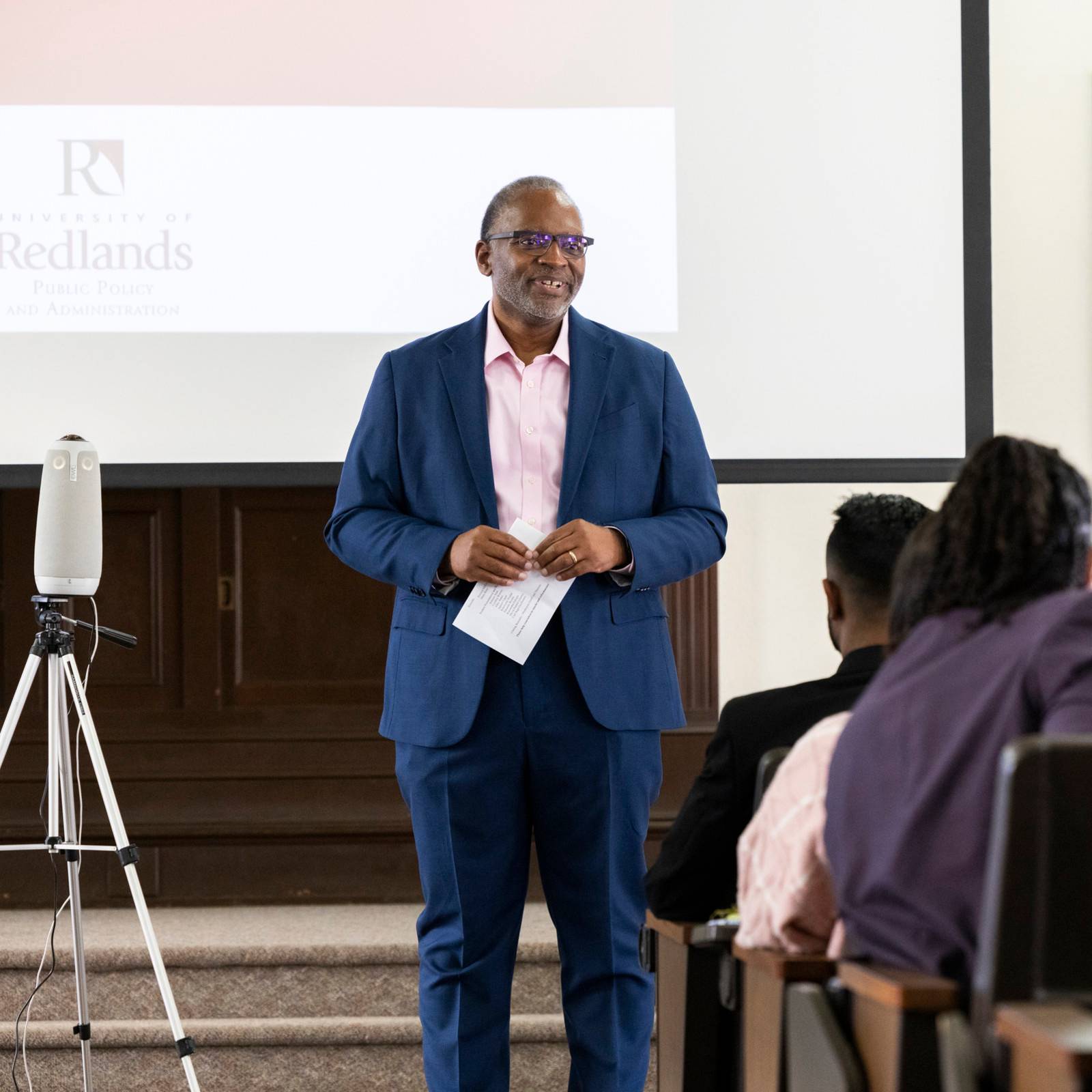 a man in a suit standing in front of a projector screen