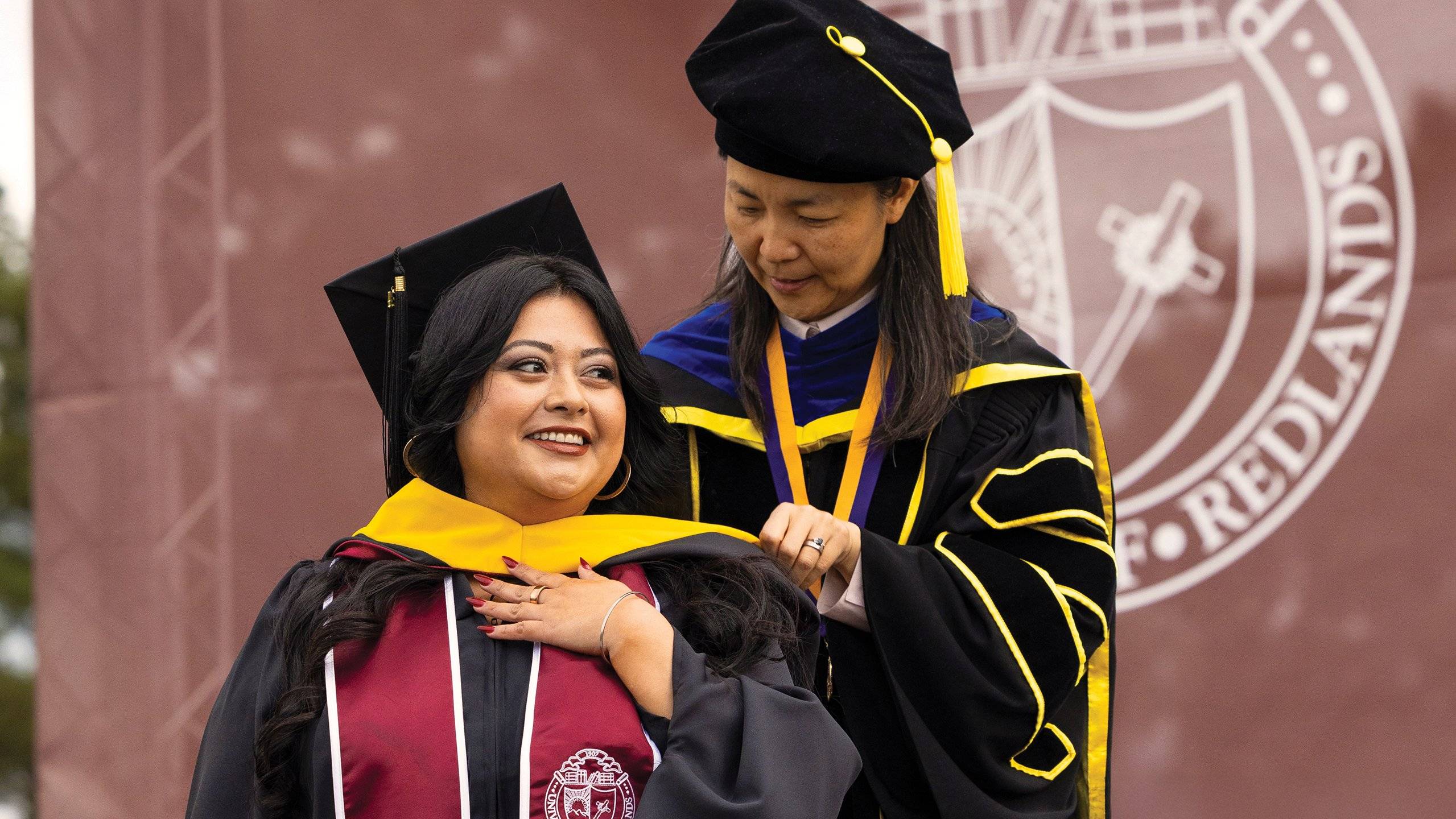A professor putting on a yellow scarf for a graduate student.