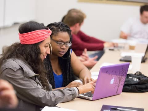 a group of people sitting at a table looking at a laptop