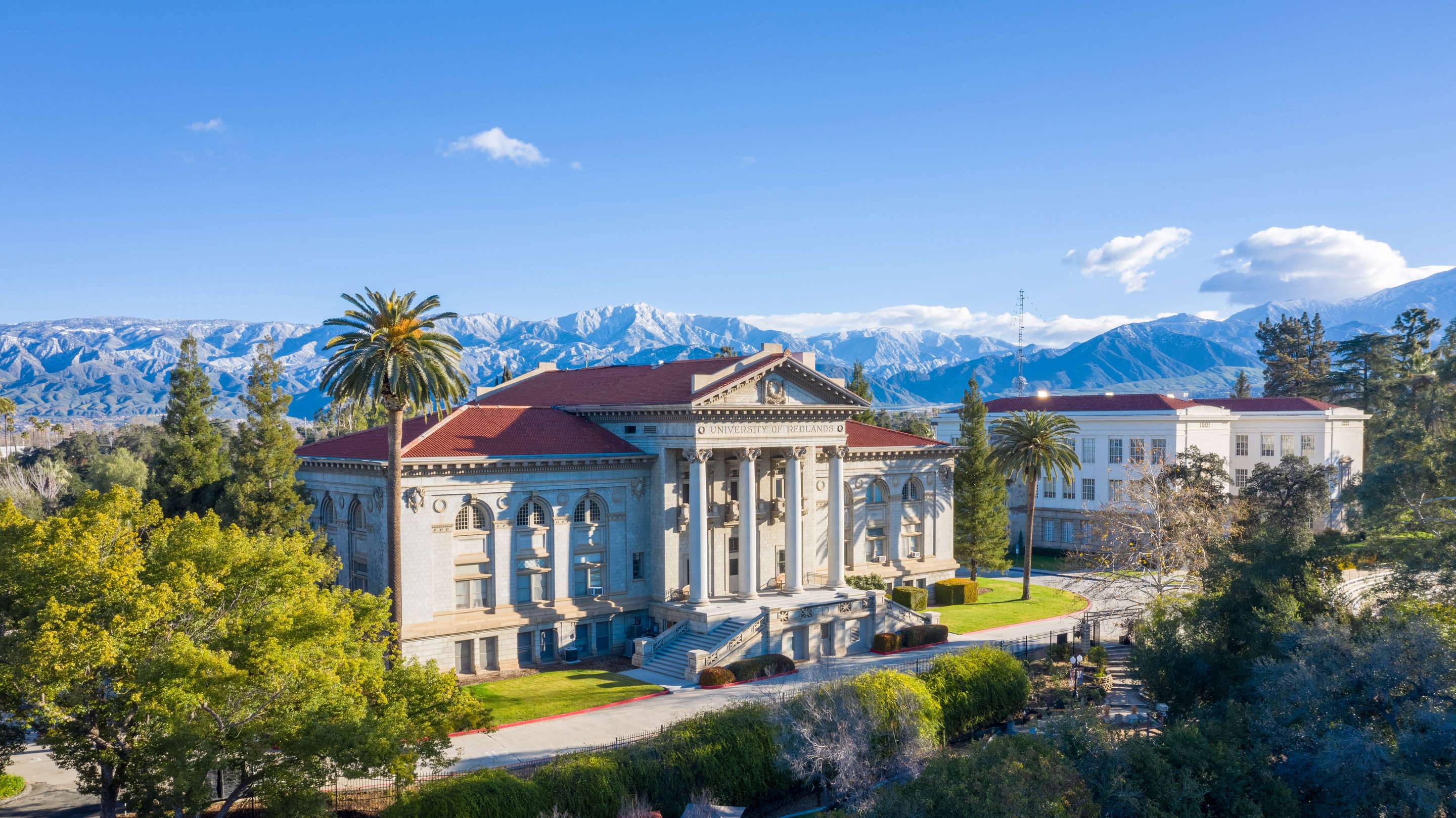 a large building with a red roof and trees and mountains in the background