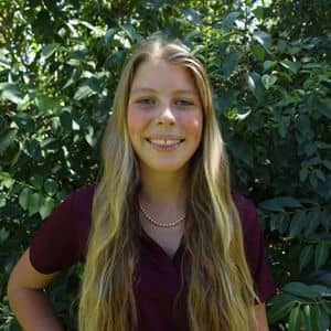a woman smiling in front of a bush