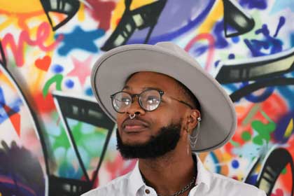 David Hazward wearing a wide-brimmed hat and glasses, standing in front of a colorful graffiti mural.