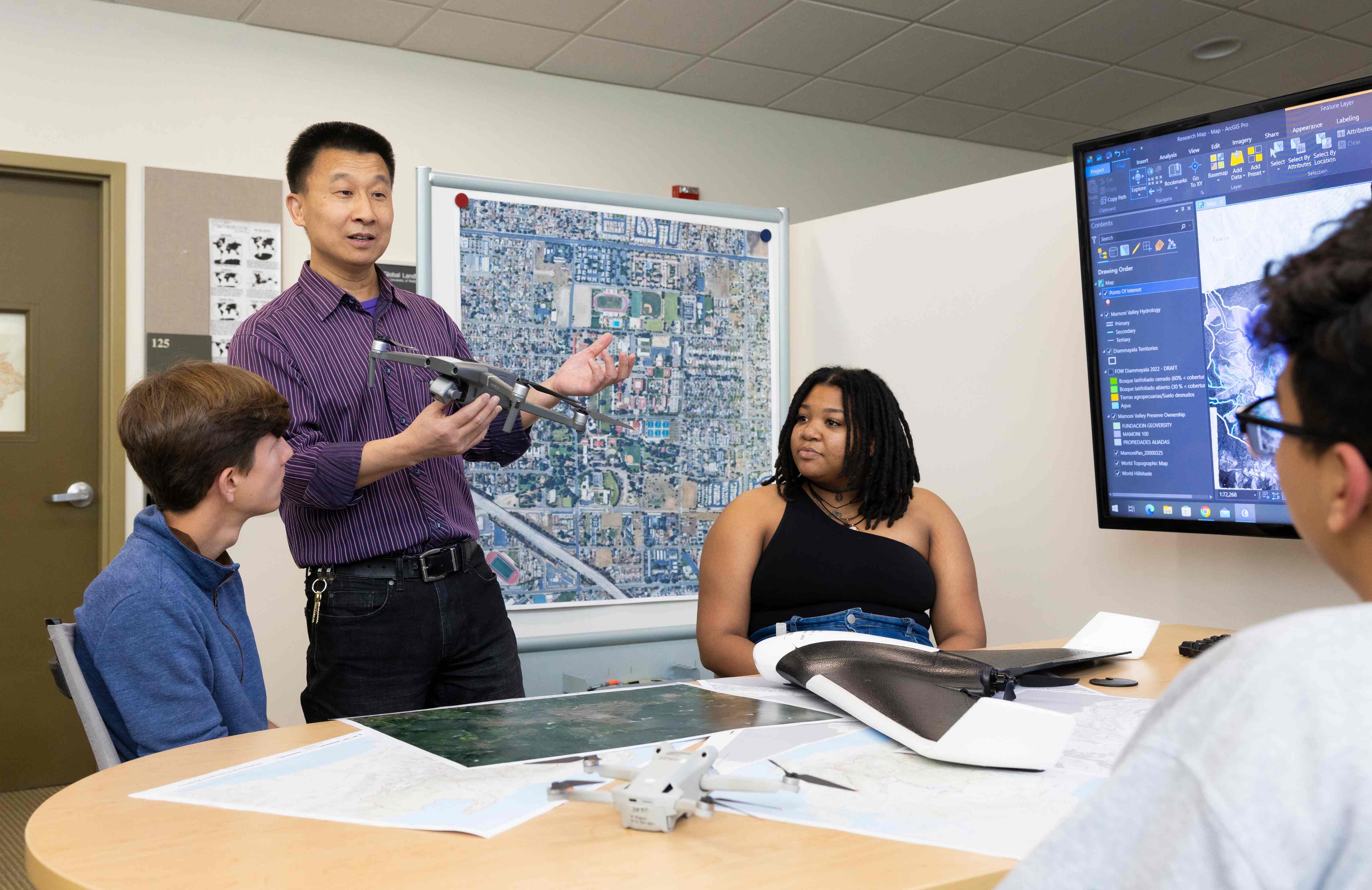 a man holding a drone and a woman sitting at a table with a large screen