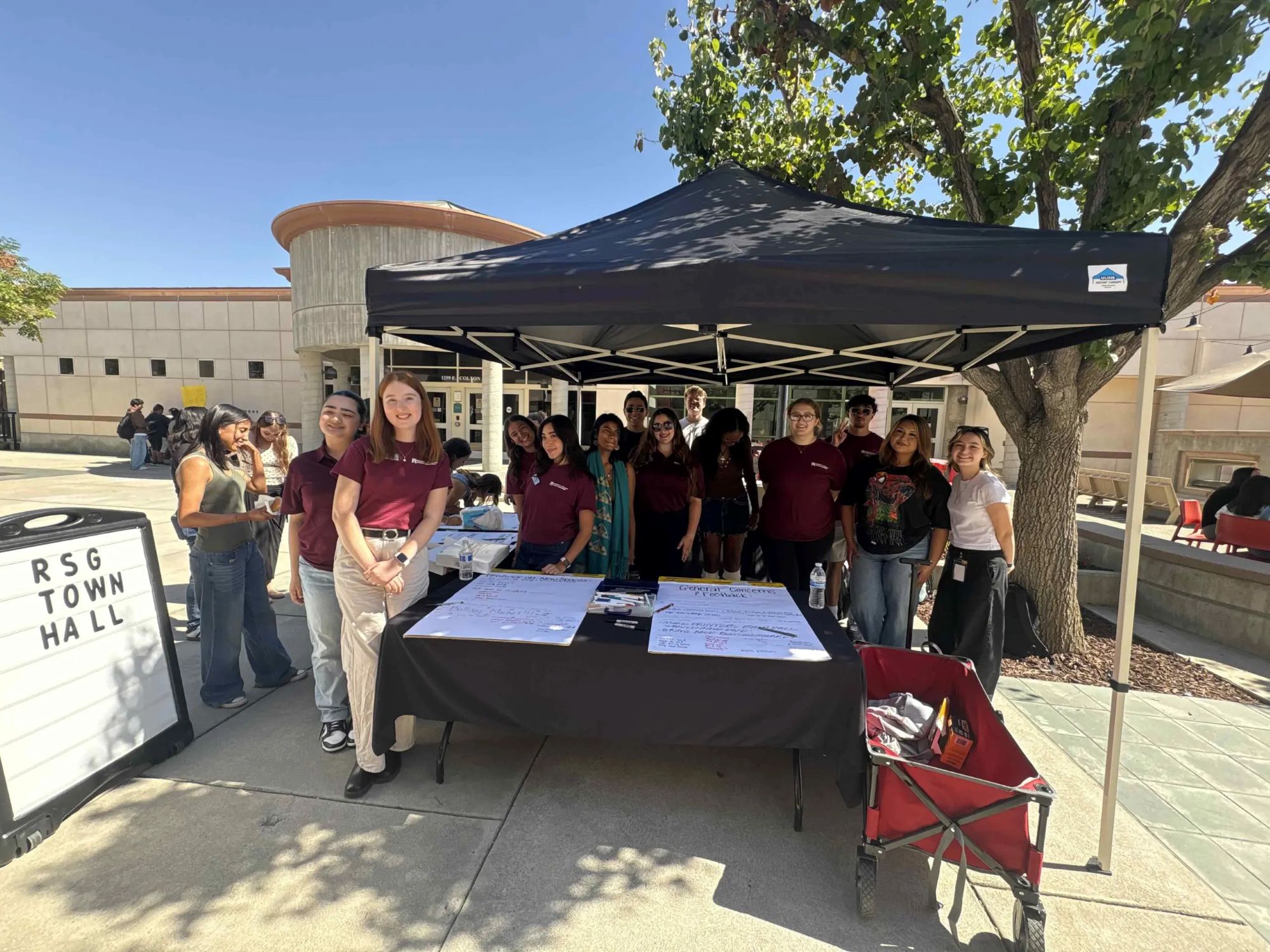 A group of Redlands Student Government members stand at a town hall booth on campus.